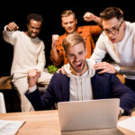 happy multicultural businesspeople showing winner gesture while working at night in office